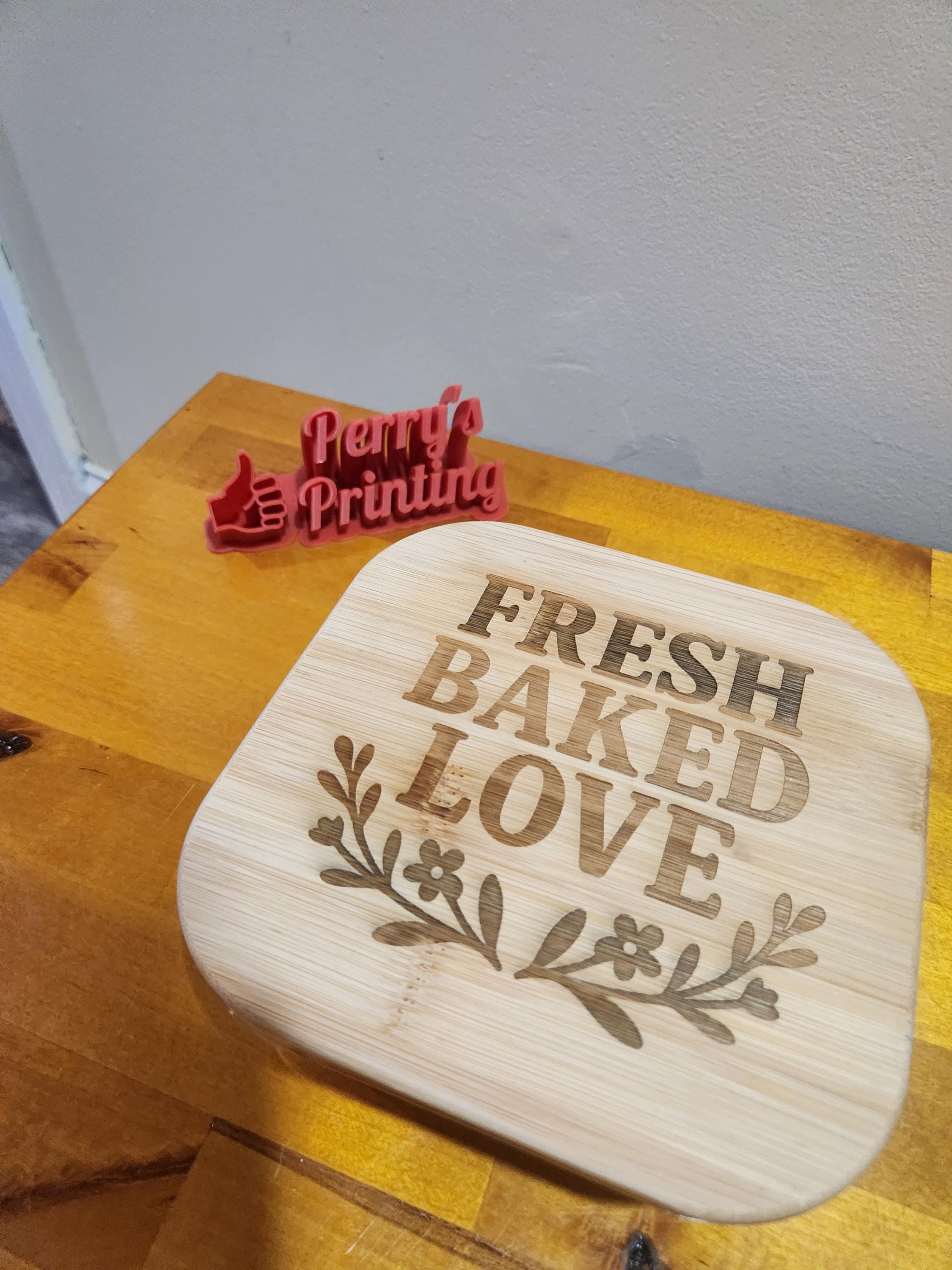 Laser engraved wooden sign with 'FRESH BAKED LOVE' and floral design on a wood table.