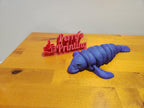 3D printed purple manatee figure and red Perry's Printing sign on wooden table