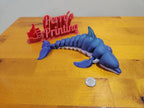 3D printed blue dolphin toy with segmented body on wooden table, red sign and coin for scale