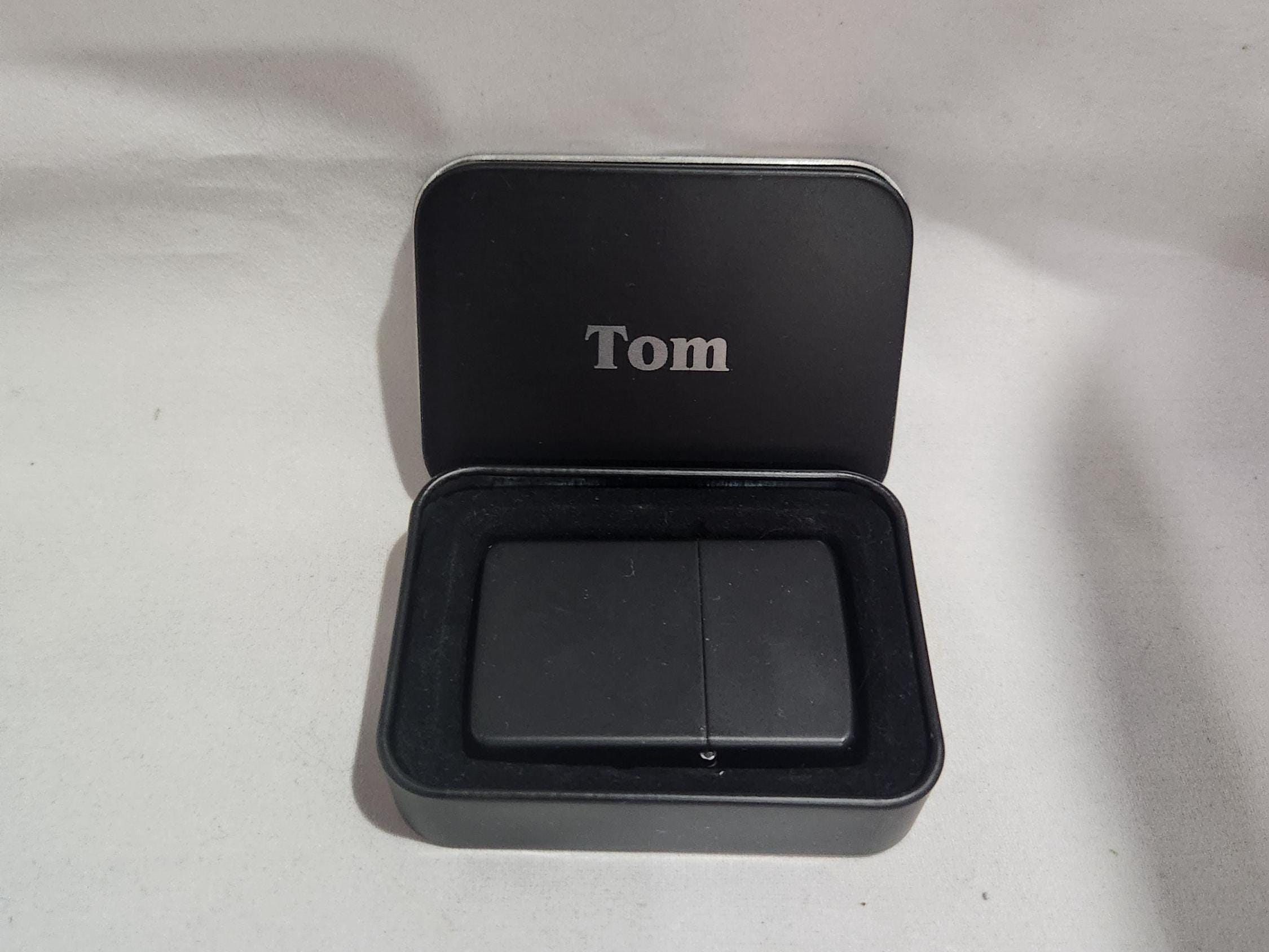 Custom engraved black lighter in a personalized metal gift box with 'Tom' inscription.