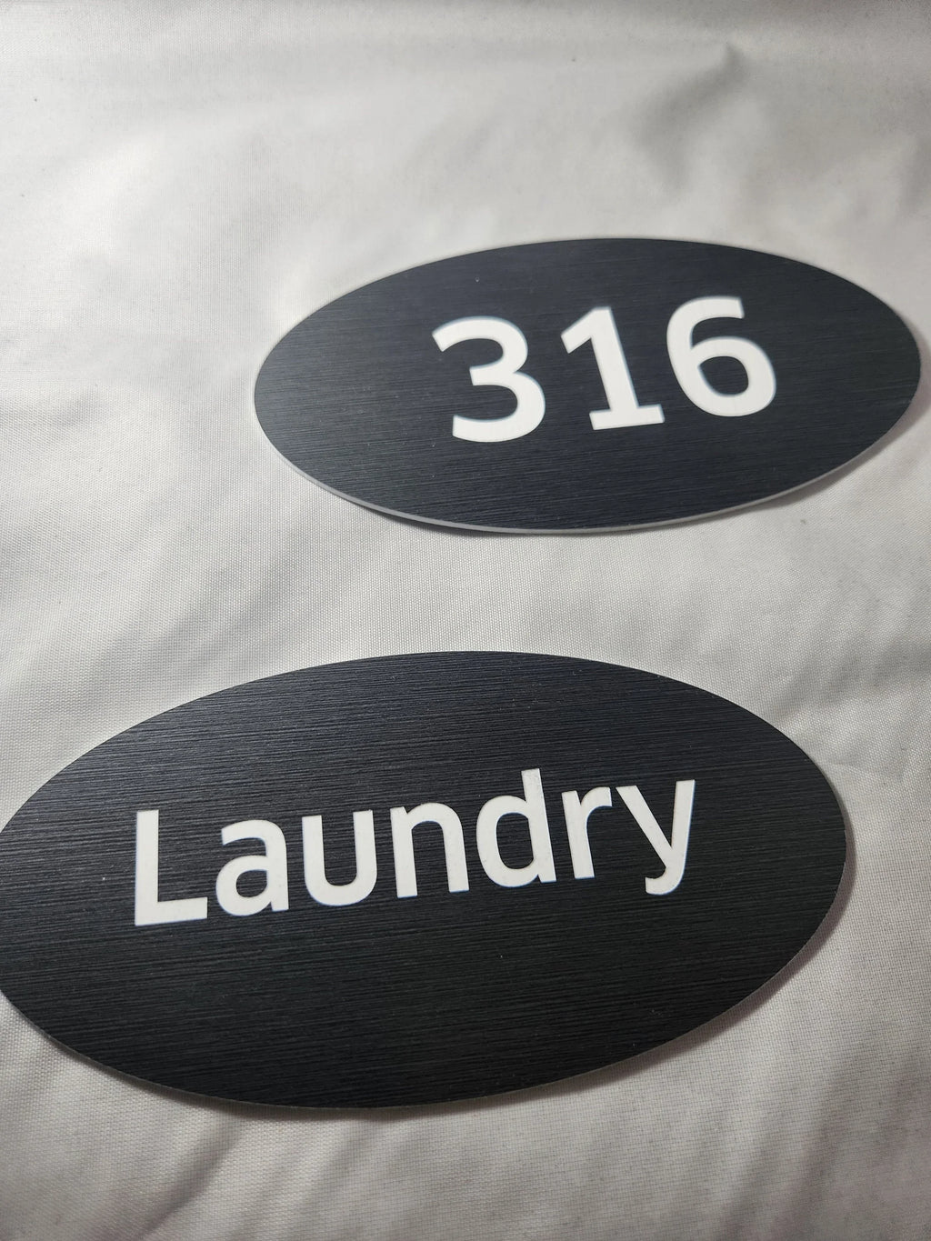 Custom black oval door signs with white text for room number 316 and laundry room