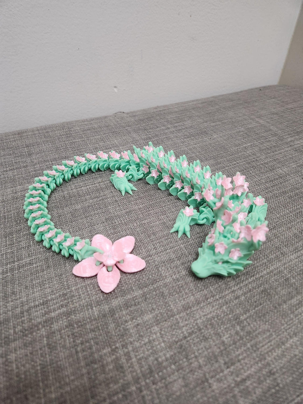 3D printed floral dragon necklace in mint green with pink flower details on grey fabric