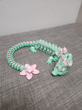 3D printed floral dragon necklace in mint green with pink flower details on grey fabric