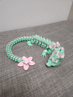3D printed floral dragon necklace in mint green with pink flower details on grey fabric