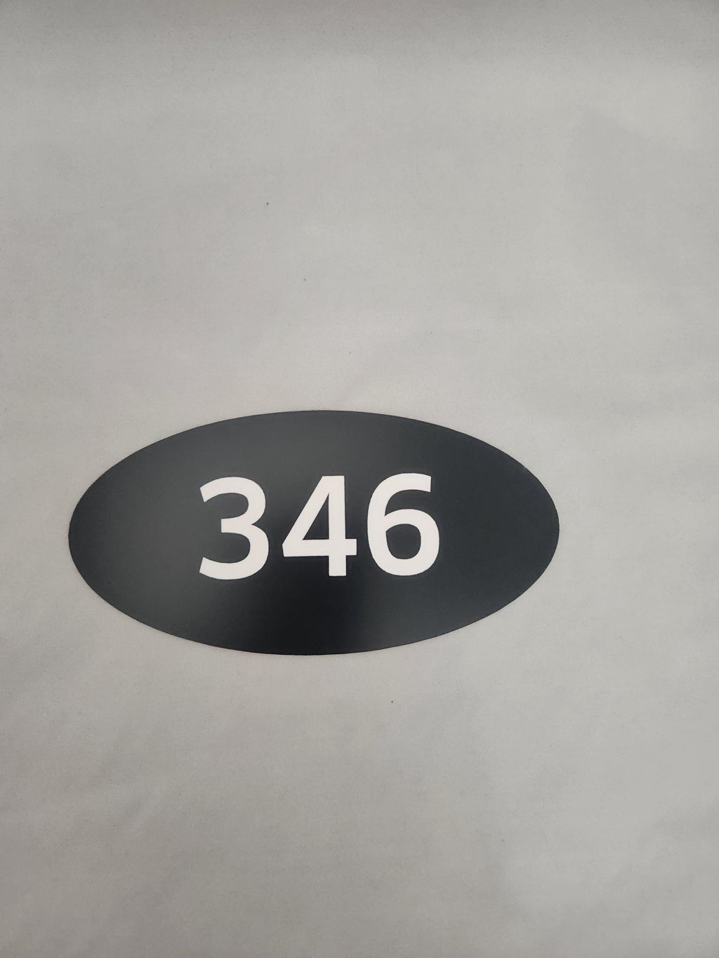 Black oval custom number sign with white 346 on a light background