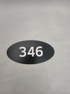 Black oval custom number sign with white 346 on a light background