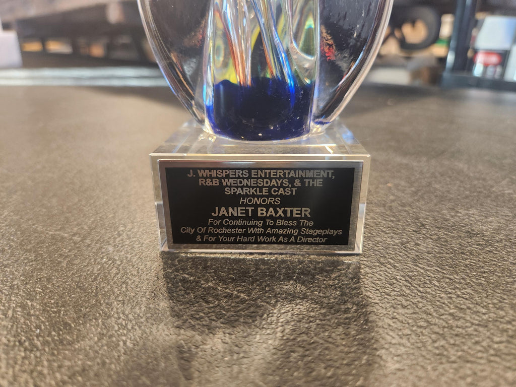 Custom engraved award with blue glass detail on a textured tabletop, honoring Janet Baxter.