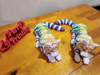 Colorful 3D printed flexible cat figures and red Perry's Printing sign on wooden table