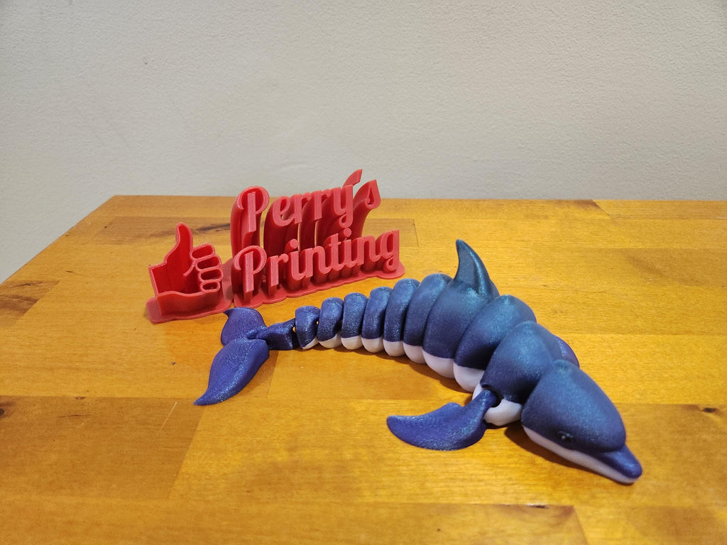 3D printed blue dolphin figurine and red Perry's Printing sign on wood table