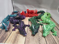 Colorful 3D printed articulated dragon models on wood surface, Perry's Printing sign in back