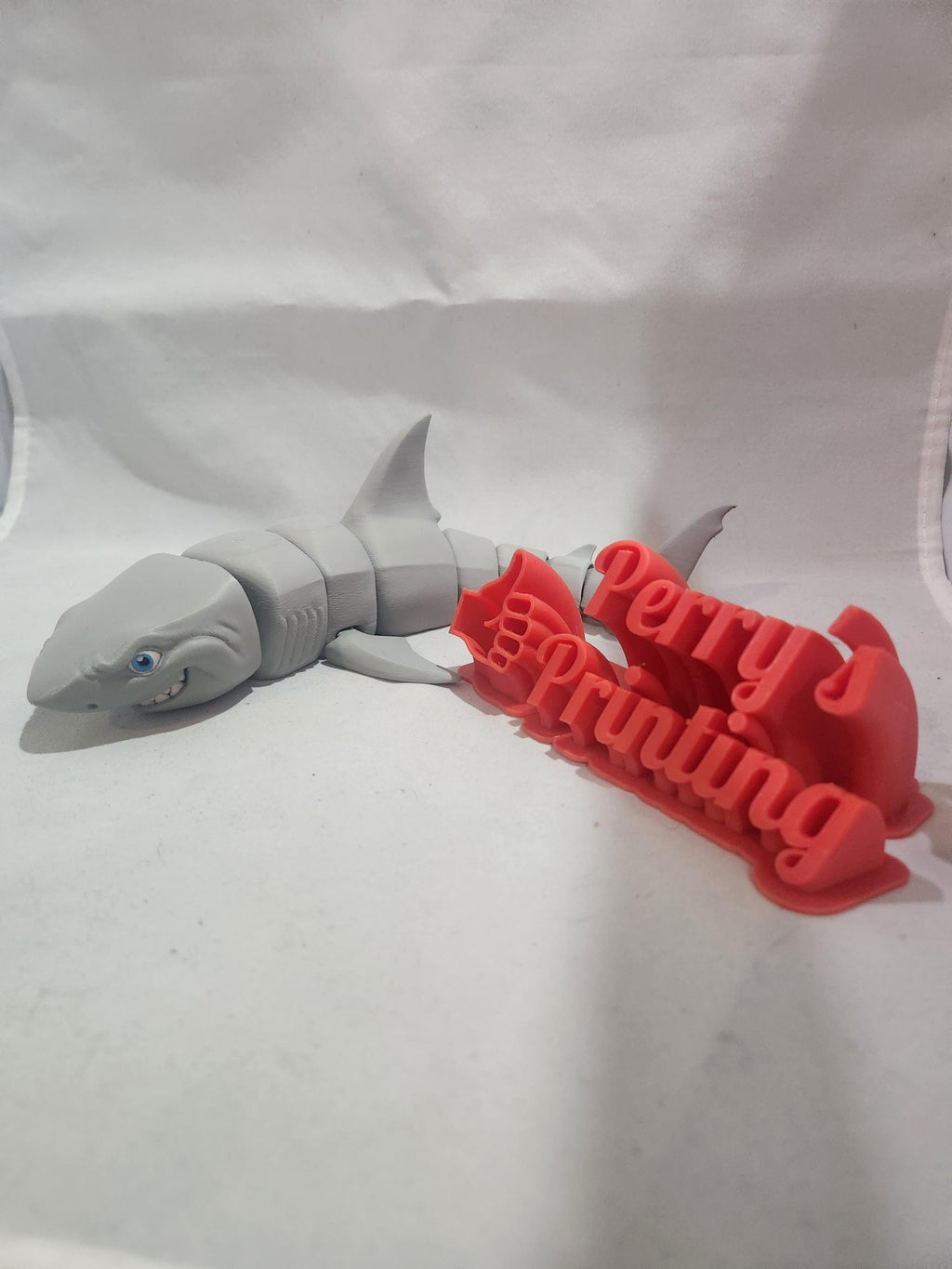 3D printed gray shark figure next to red 3D text sign on white background