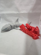 3D printed gray shark figure next to red 3D text sign on white background