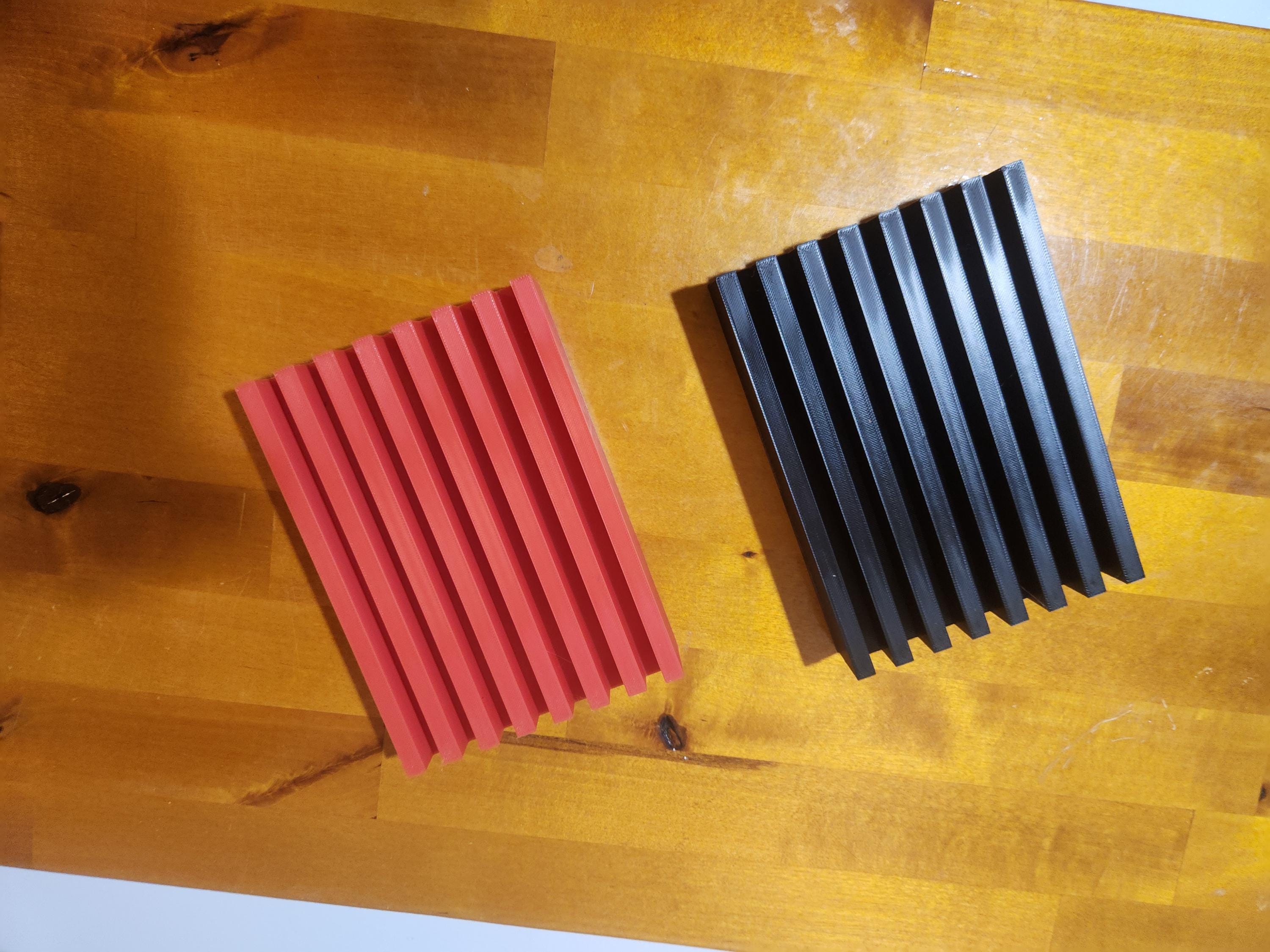 Red and black 3D printed slotted panels on a wooden surface, custom plastic parts