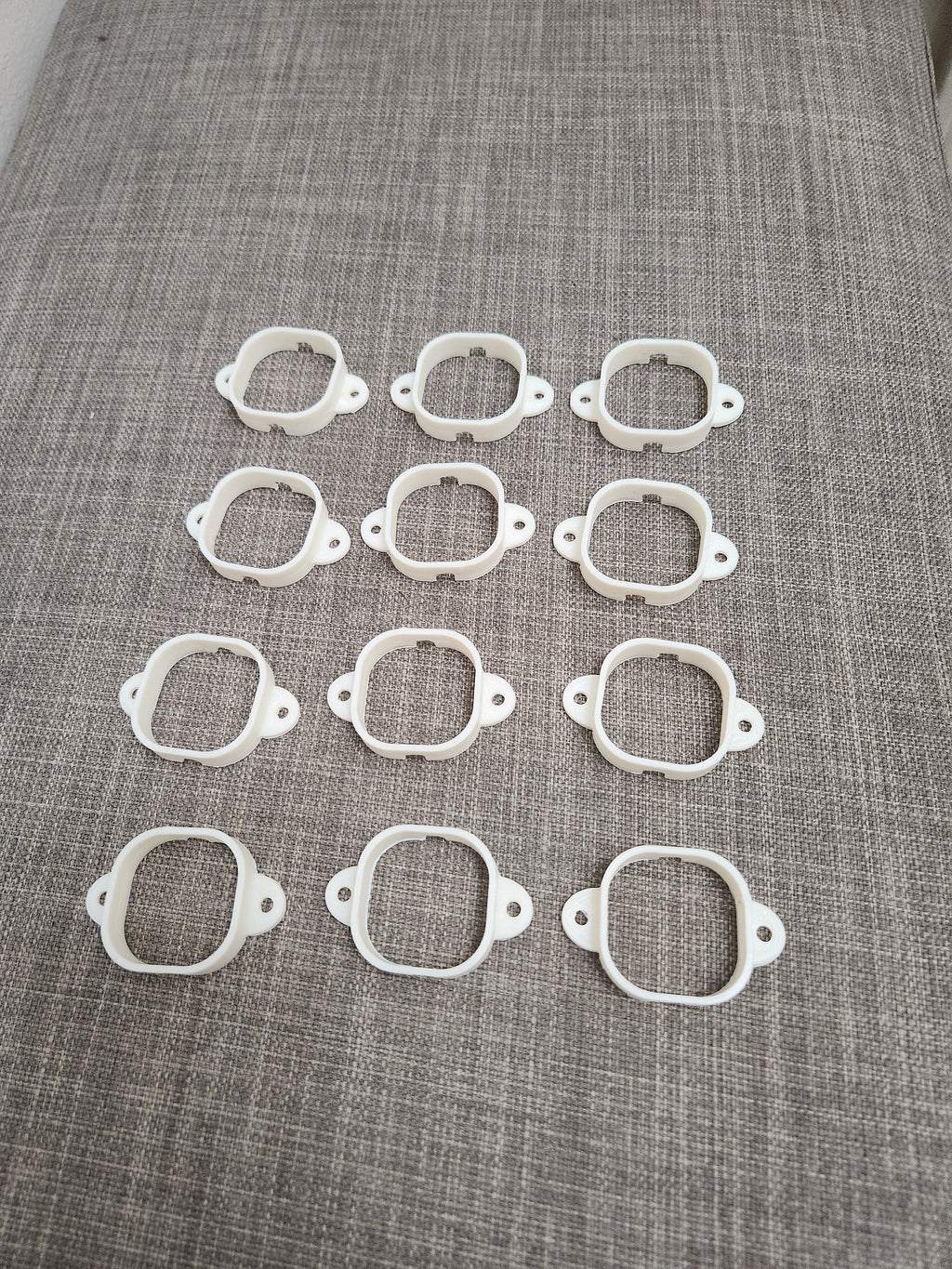 Twelve white 3D printed plastic mounting brackets arranged on a gray fabric surface
