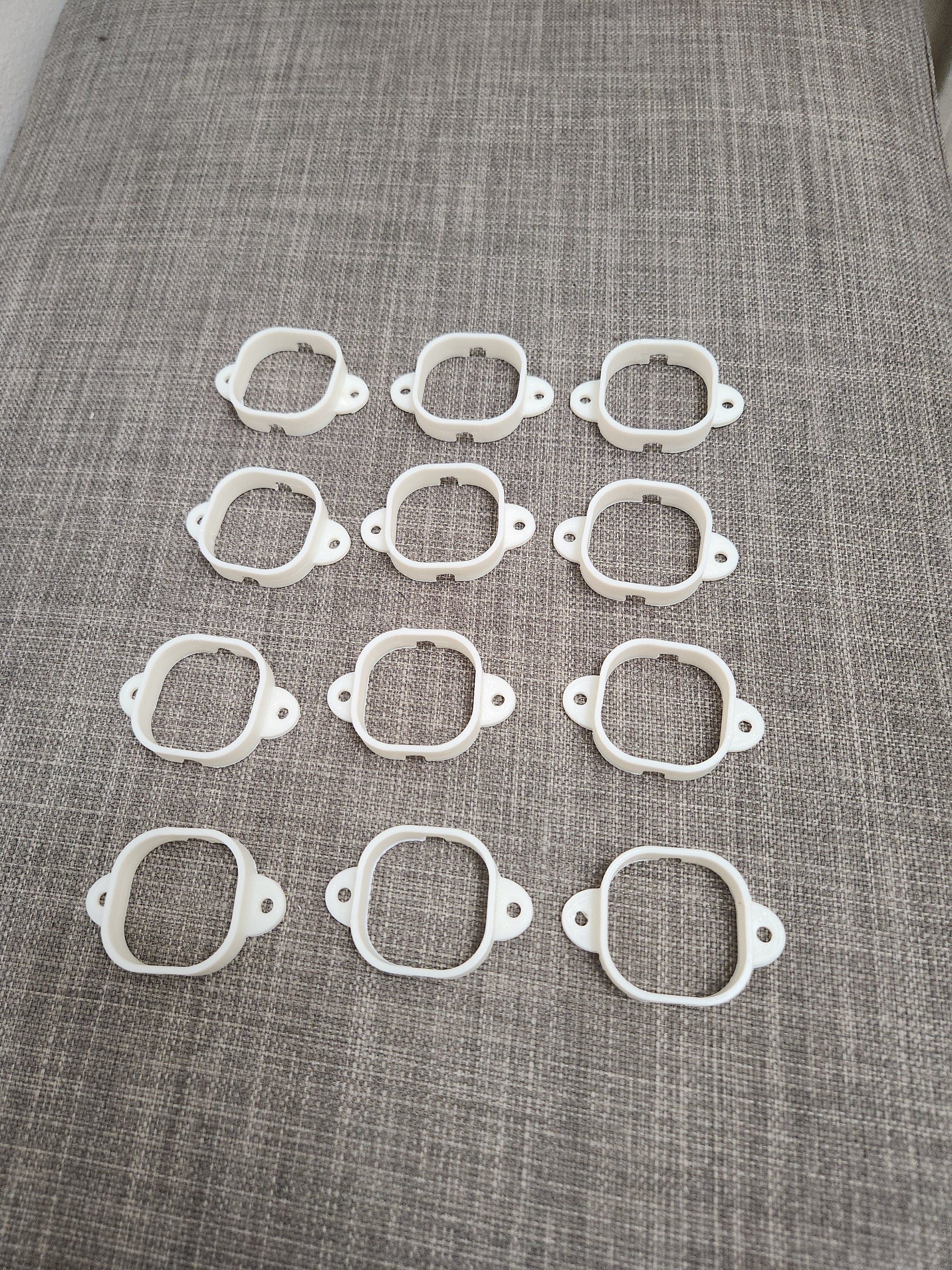 Twelve white 3D printed plastic mounting brackets arranged on a gray fabric surface