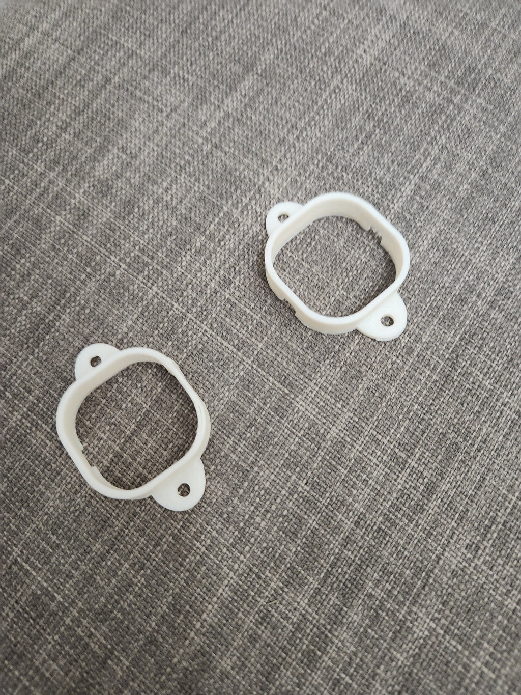 Two white 3D printed plastic mounting brackets on a gray textured fabric surface