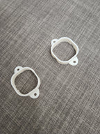 Two white 3D printed plastic mounting brackets on a gray textured fabric surface
