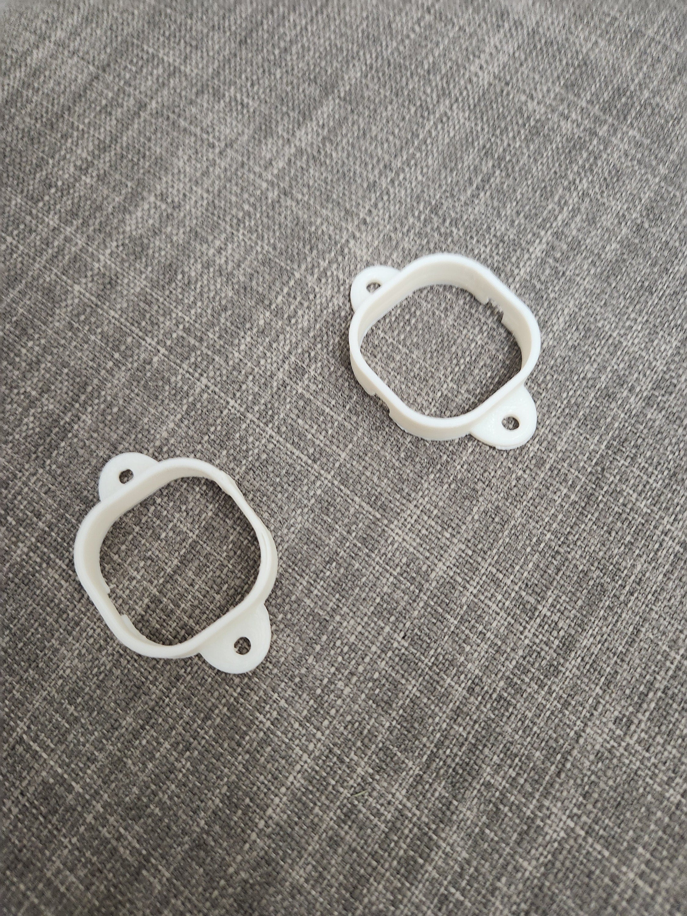 Two white 3D printed plastic mounting brackets on a gray textured fabric surface