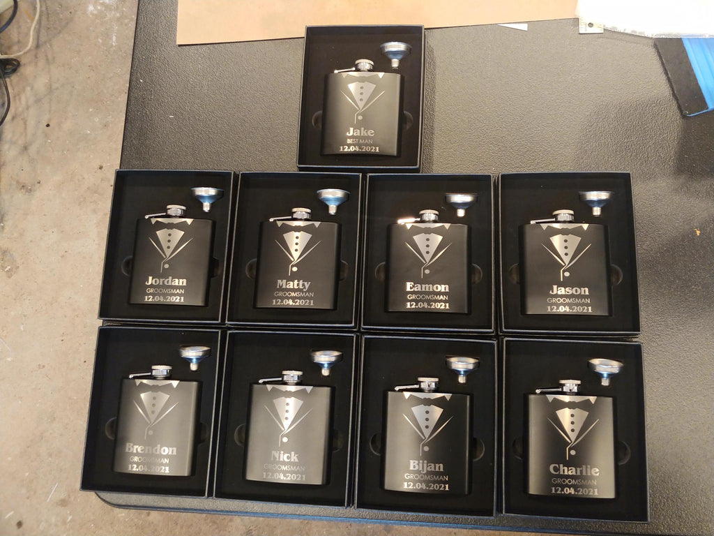 Custom engraved black groomsmen flasks with tuxedo design in gift boxes, wedding party favors.