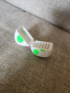 3D printed white and green egg-shaped case with open lid on beige fabric