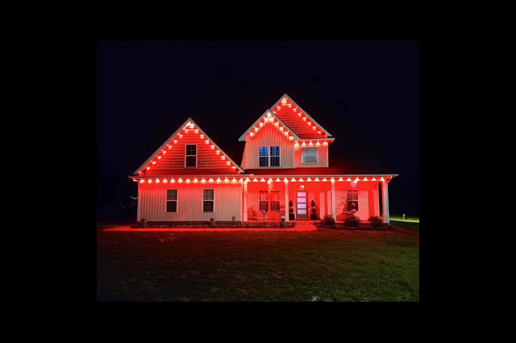 Two-story house at night with bright red LED holiday lights outlining the roof and porch