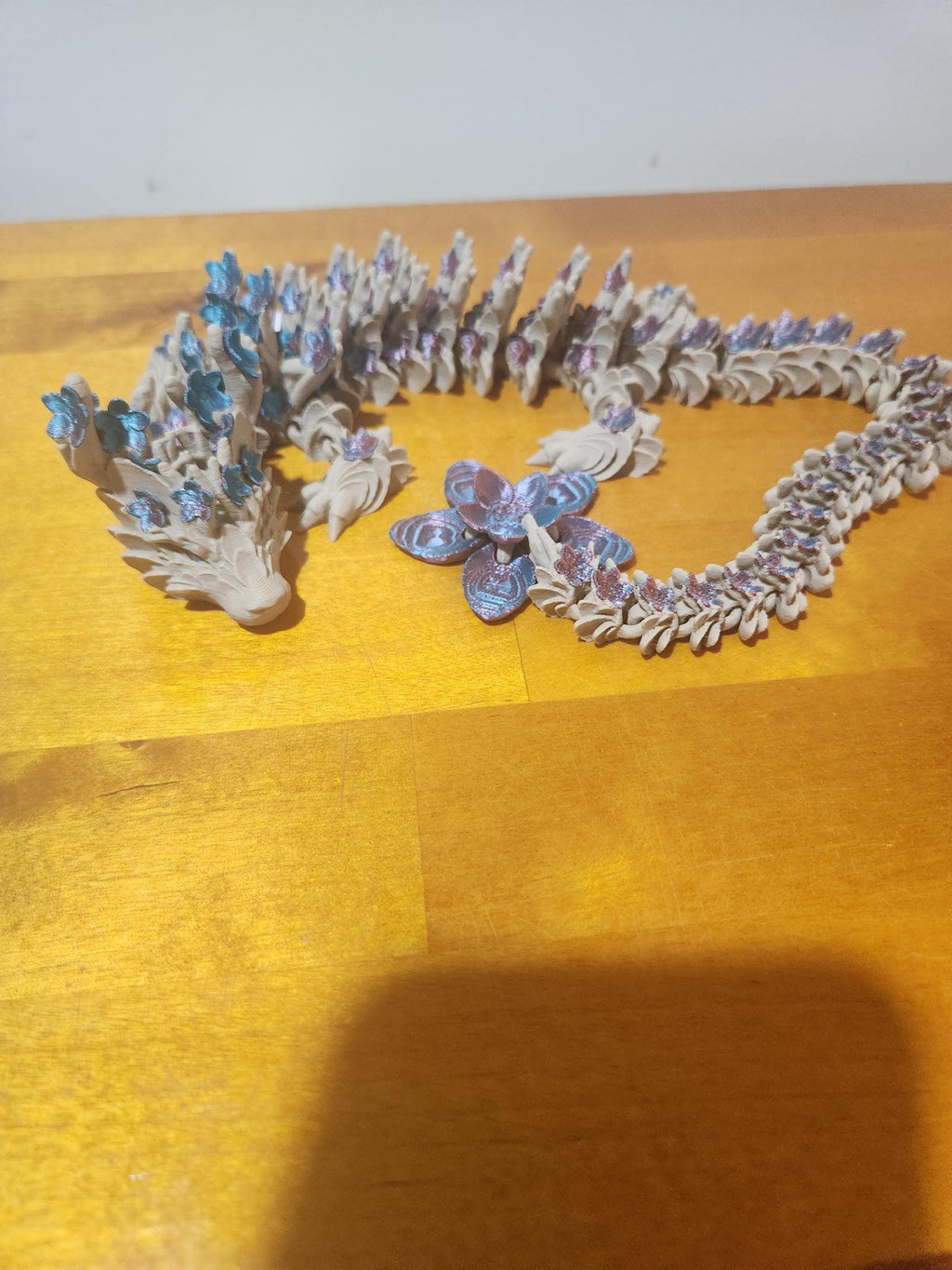 3D printed dragon figurine with blue and purple floral details on wooden surface