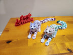 Two colorful 3D printed snow leopard figurines on wood table with red 'Printing' sign