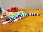 Colorful 3D printed articulated tiger figurine on wooden table, custom signage in background