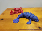 3D printed flexible blue manatee figurine and red Perry's Printing sign on wooden table