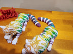 Colorful 3D printed articulated cat figurines with striped tails on a wooden surface.