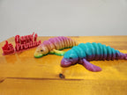 3D printed rainbow manatee figurines and red Perry's Printing sign on wooden table