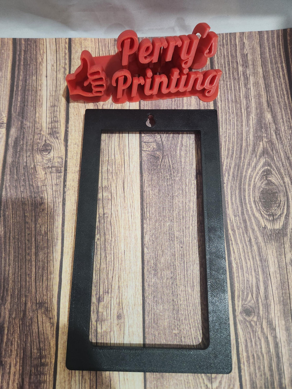3D printed red sign with 'Perry's Printing' and black rectangular frame on wood surface