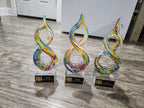 Colorful glass infinity-shaped awards with engraved plaques on a wood floor